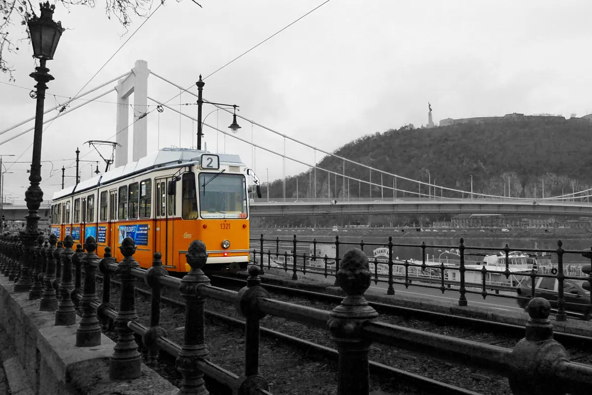 Žlutá tramvaj číslo 2 na pešťském nábřeží, za ní most přes Dunaj a vrch Gellért.